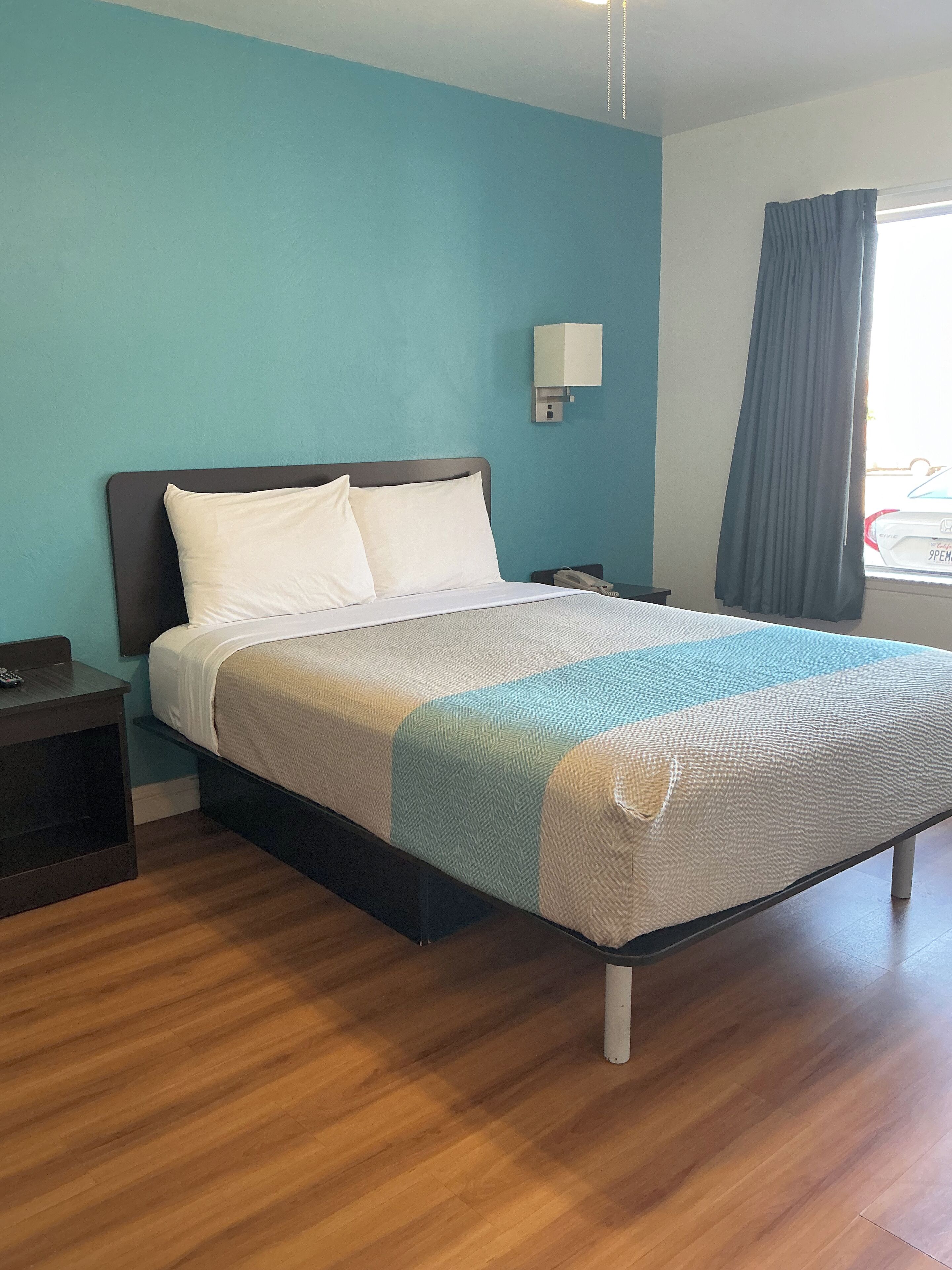 Habitación de hotel con cama, mesita de noche, lámpara de pared y ventana con cortinas.