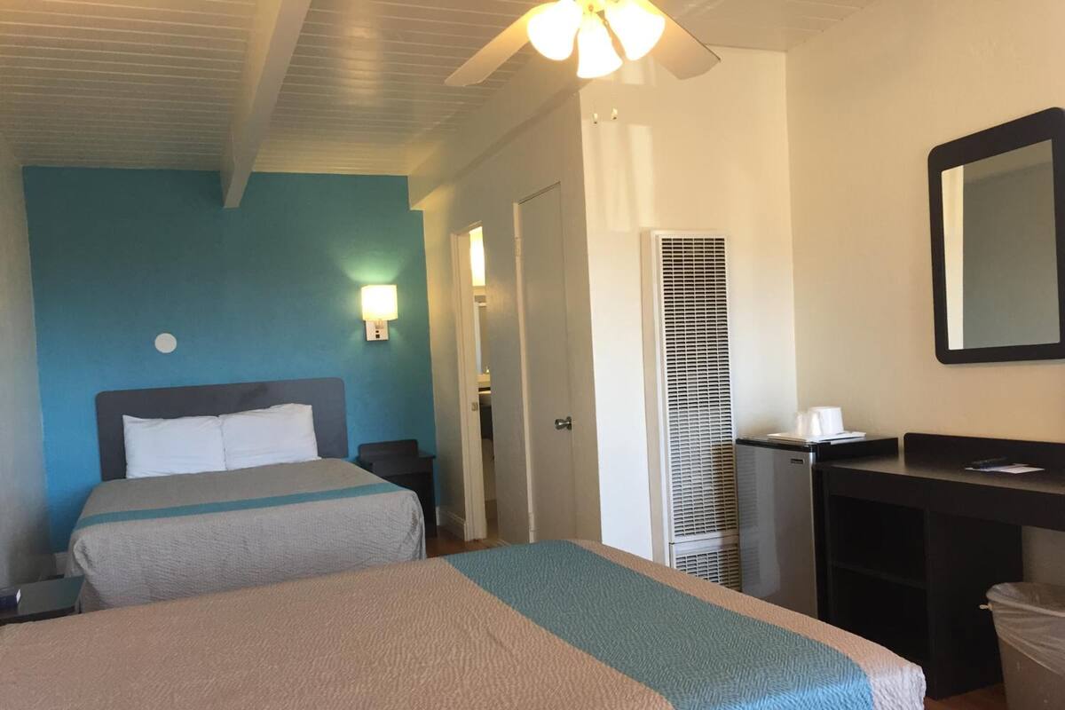 Una habitación de hotel con dos camas, un escritorio, un espejo y un ventilador de techo.