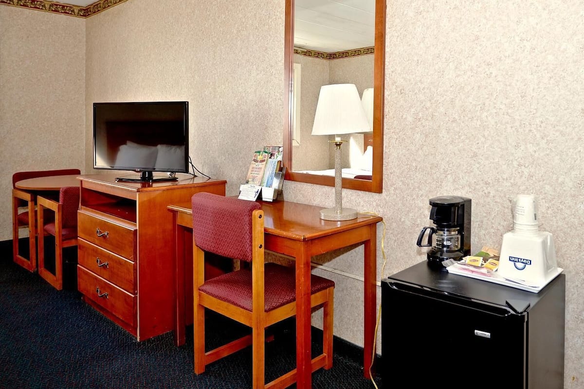 Ein Hotelzimmer mit einem Holztisch, einem Fernseher, einer Lampe, einer Kaffeemaschine und einer Minibar.
