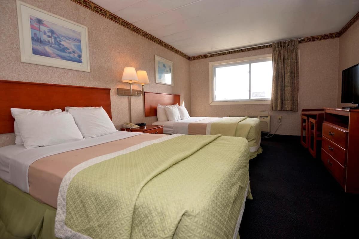 Ein Hotelzimmer mit zwei Betten, einem Schreibtisch, einem Fernseher und einem Fenster mit Vorhängen.