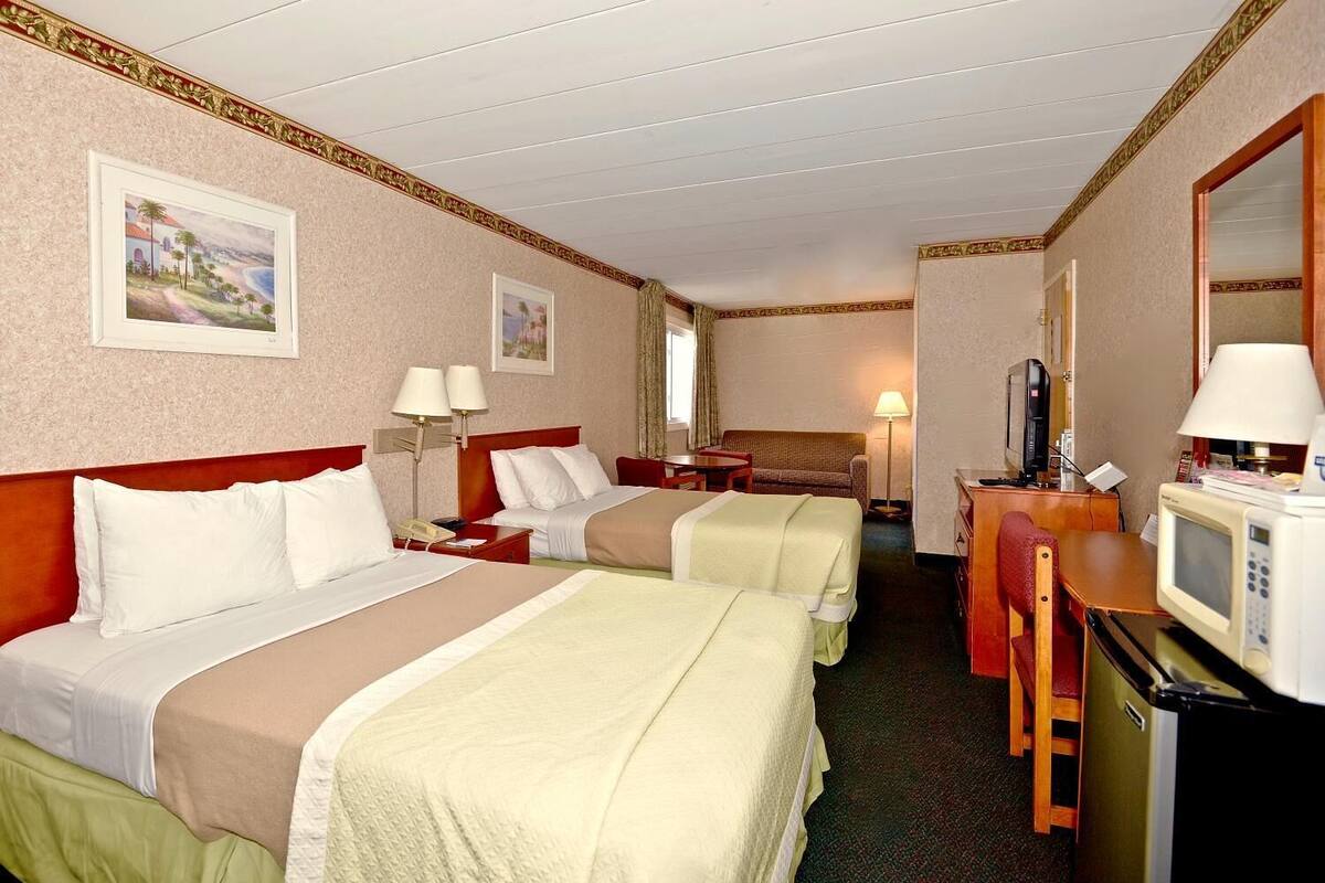 Ein Hotelzimmer mit zwei Betten, einem Schreibtisch mit Computer, einem Fernseher und einer Mikrowelle.