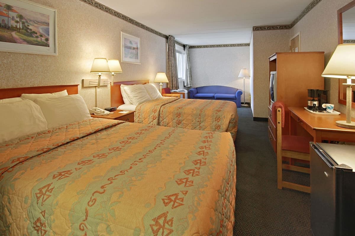 Ein Hotelzimmer mit zwei Betten, einem Schreibtisch, einem Stuhl, einer Kaffeemaschine und einem Fernseher.