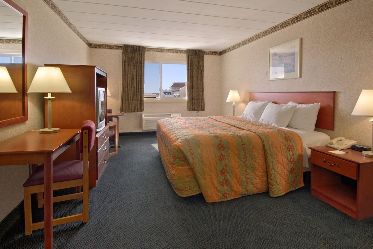 Ein Hotelzimmer mit Bett, Schreibtisch, Stuhl, Fernseher und einem Fenster mit Vorhängen.