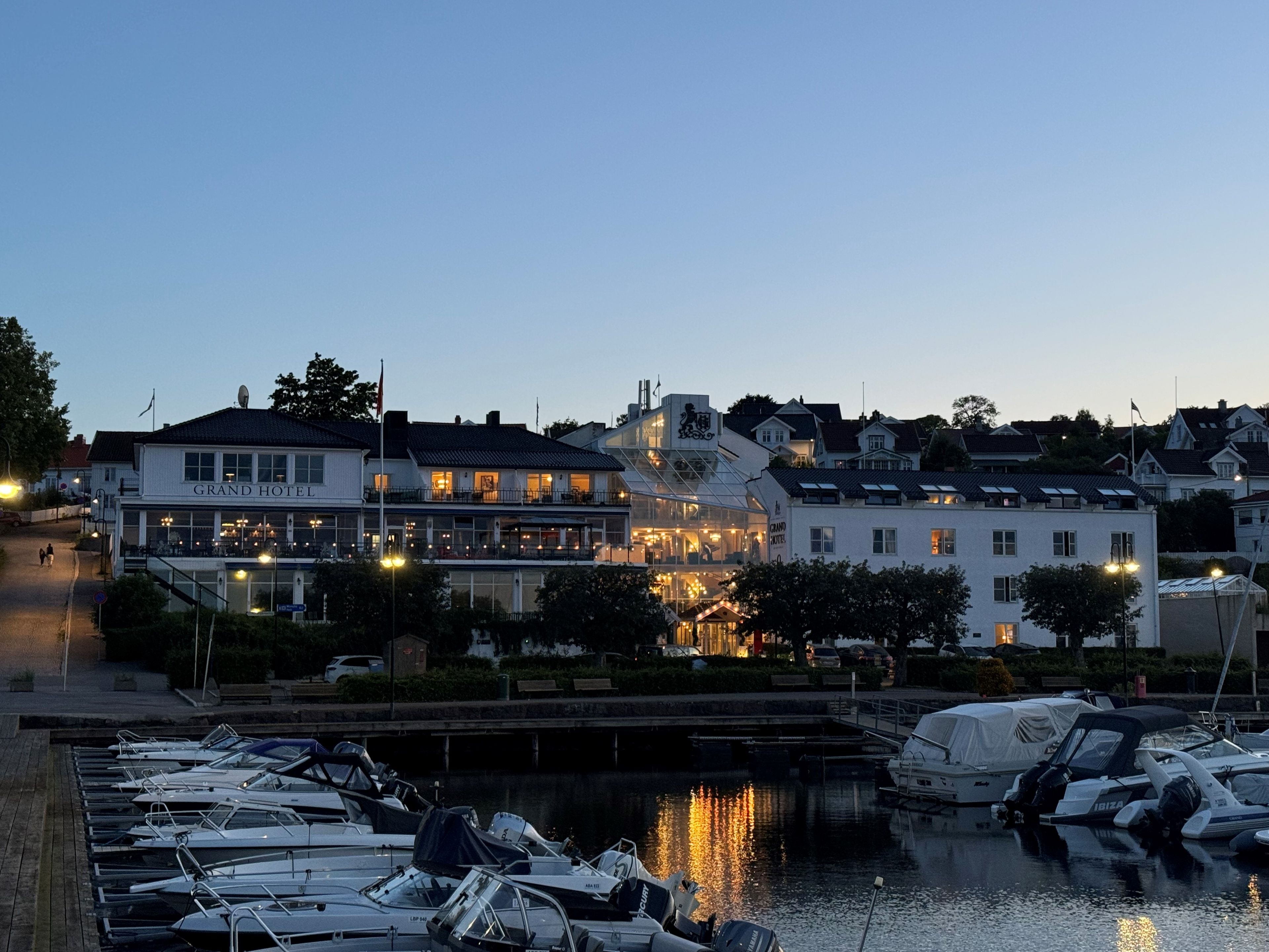 Una marina con barcos amarrados, un edificio frente al agua con un letrero que dice 'Grand Hotel' y un puente al fondo.