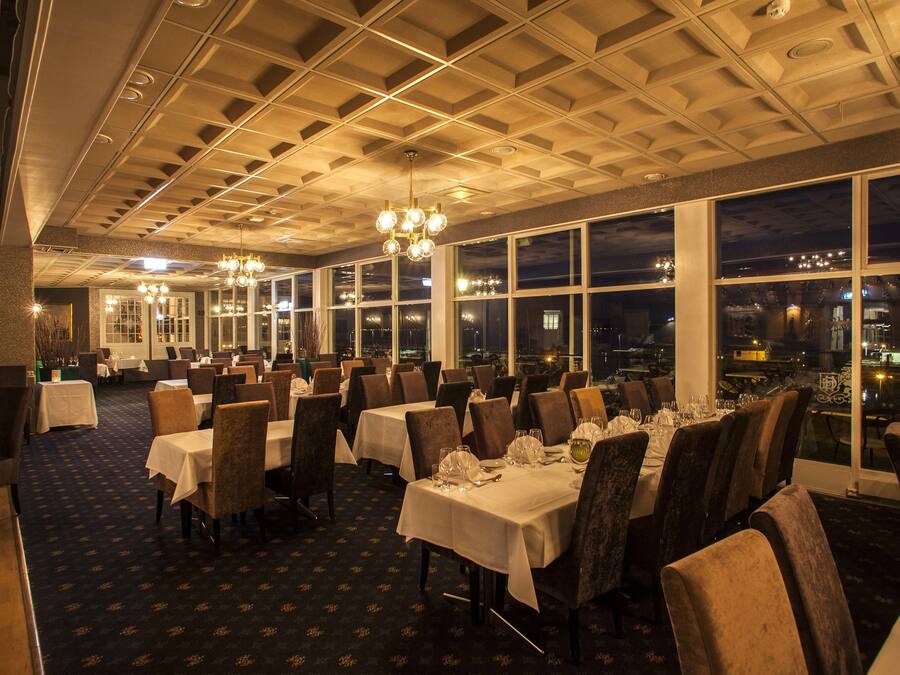 A restaurant with tables set for dining, large windows, and a city view at night.