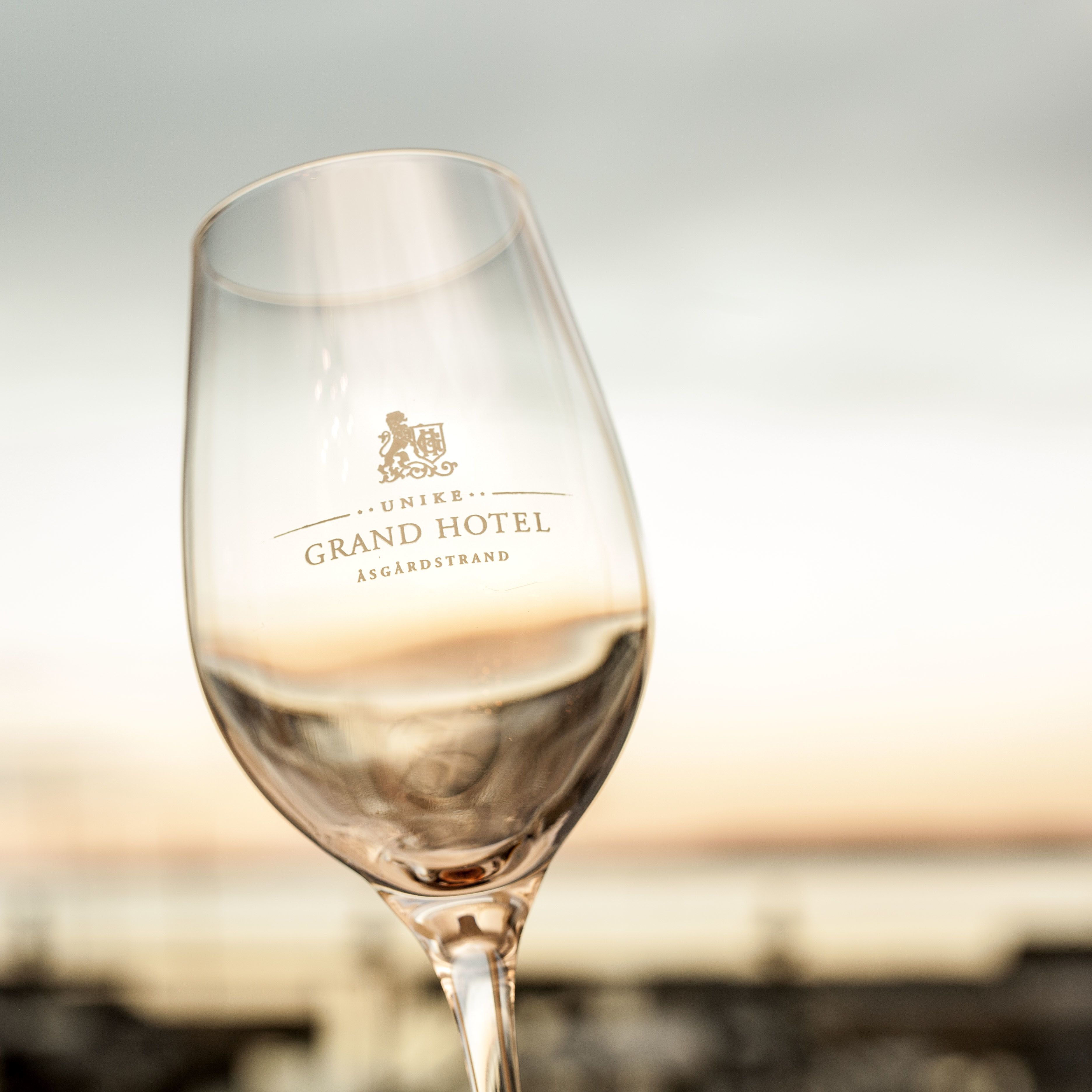 A champagne flute with the inscription "UNIKE GRAND HOTEL ASGARDSTRAND" on its base.
