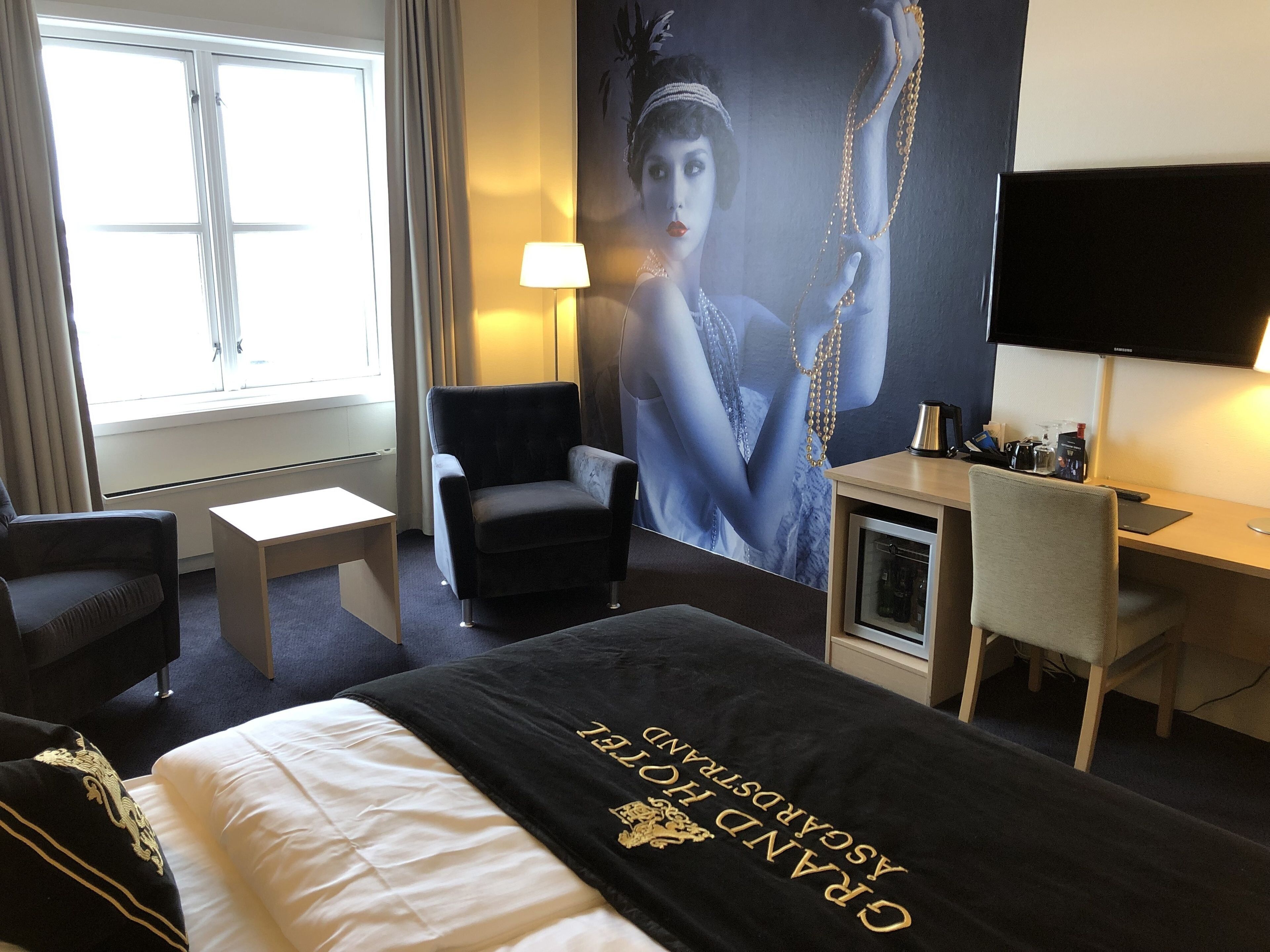 Una habitación de hotel con cama, escritorio, silla, televisor y un cartel grande en la pared.