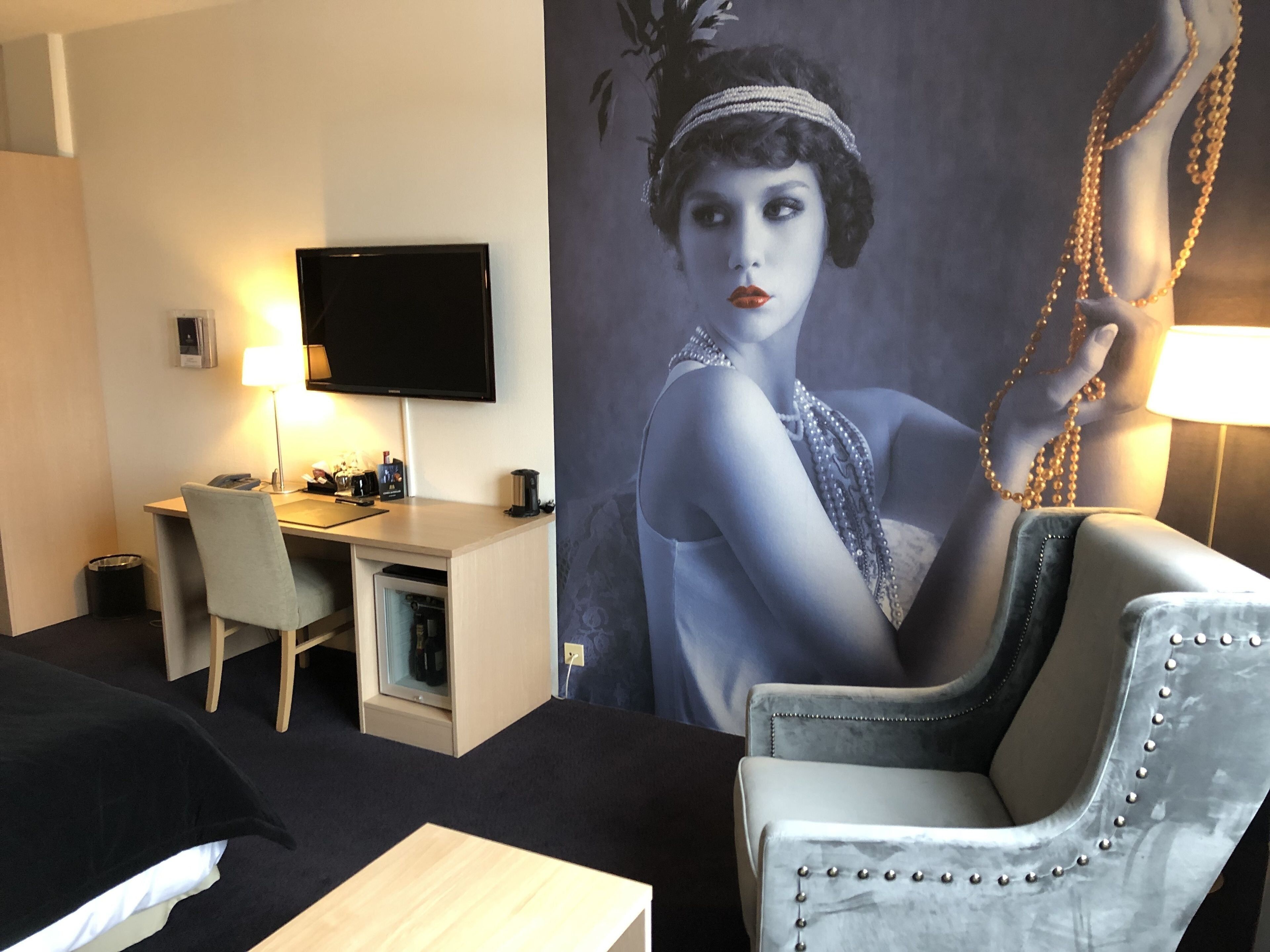A hotel room with a bed, a desk, a chair, a television, and a large wall mural.