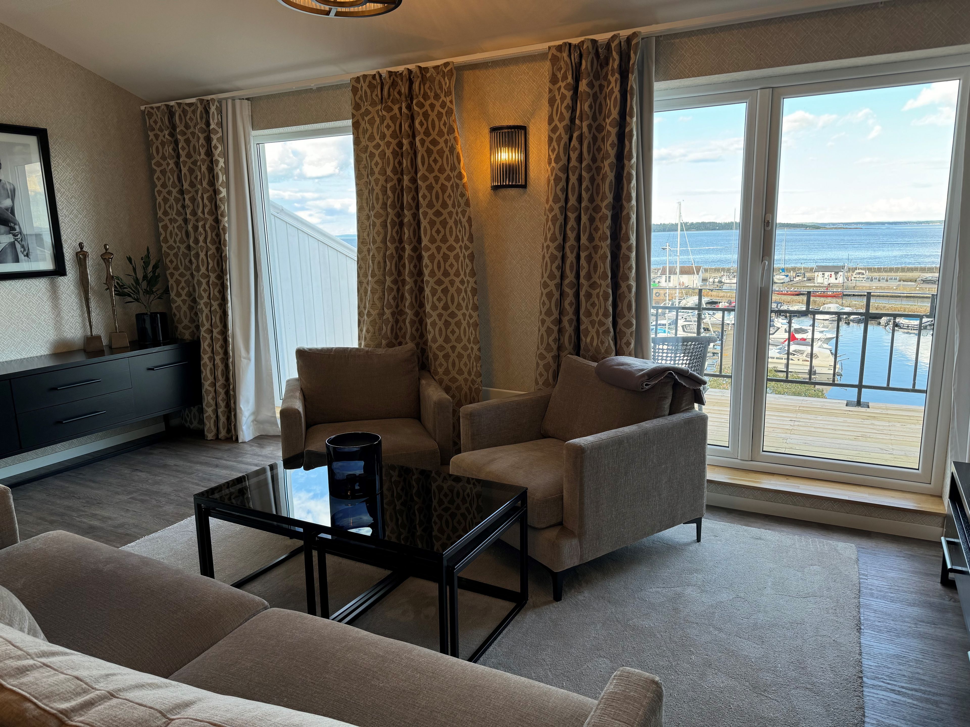 Ein Hotelzimmer mit einer Couch, Sesseln, einem Couchtisch und Blick auf das Meer und Boote.