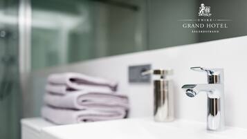 Un baño moderno con un lavamanos blanco, dos grifos cromados y toallas ordenadamente dobladas.