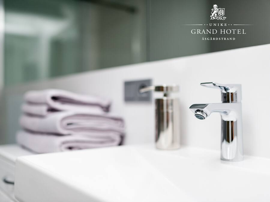 Un baño moderno con un lavamanos blanco, dos grifos cromados y toallas ordenadamente dobladas.