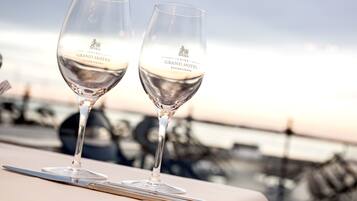 Dos copas de vino con la inscripción "UNIKe. GRAND HOTEL ASGARDSTRAND" sobre una mesa, con vista al mar y embarcaciones al fondo.