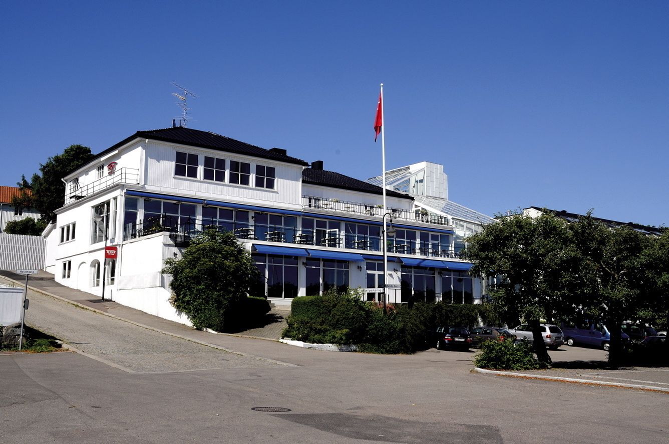 Un edificio de dos pisos con fachada blanca, ventanas grandes y una bandera roja en la parte superior.