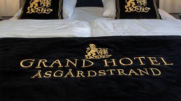 A bed with a black cover featuring the Grand Hotel Åsgårdstrand logo and name.