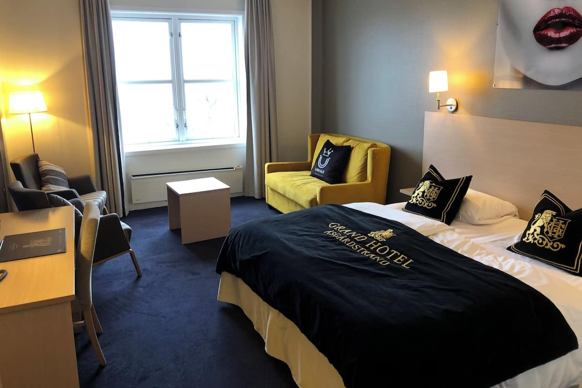 A hotel room with a bed, a desk, a chair, a small table, and a window with curtains.