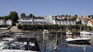 A marina with boats docked, a building with a sloped roof, and a clear sky. - Grand Hotel Åsgårdstrand - Unike Hoteller (Horten)