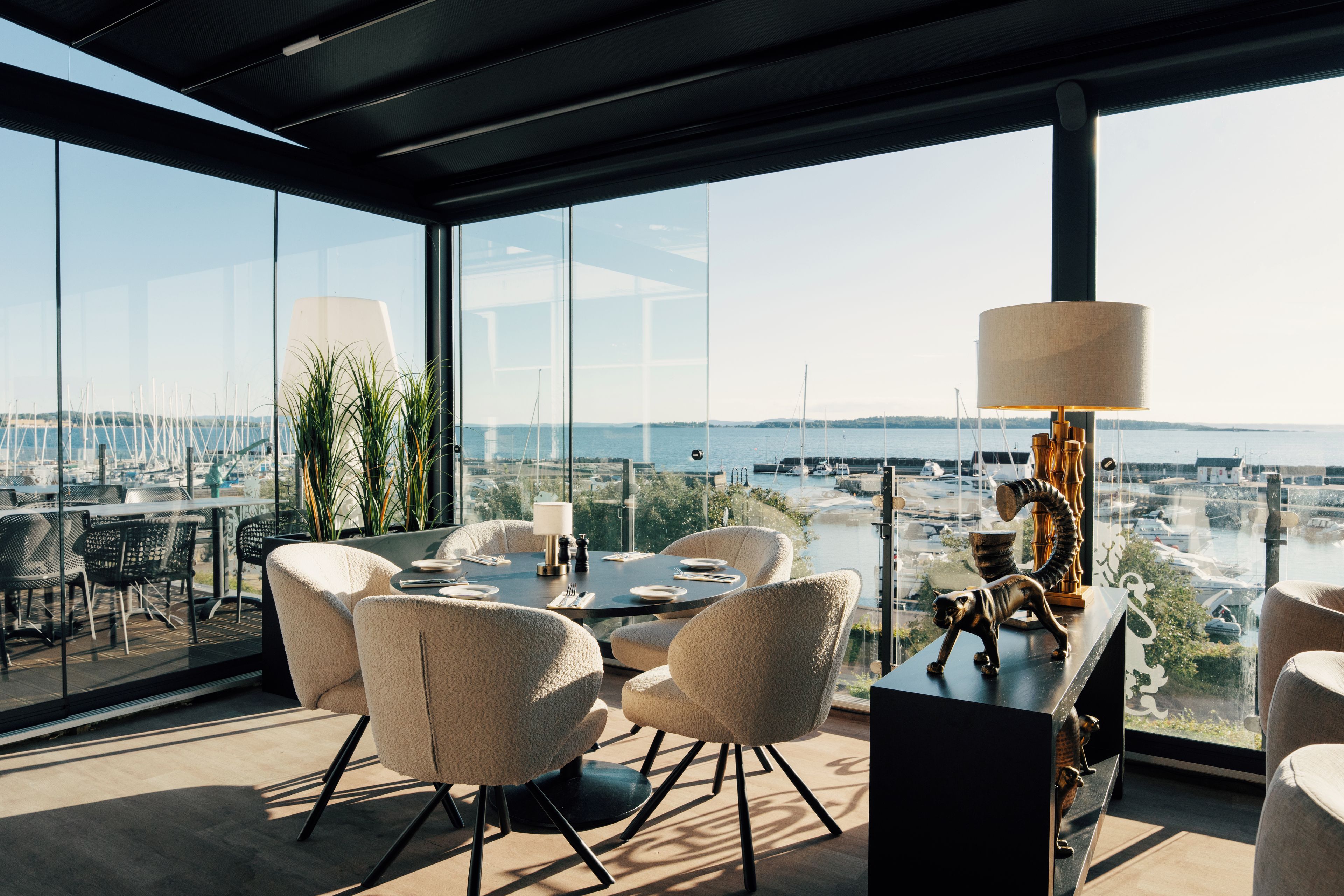 Un espace repas moderne offrant une vue panoramique sur un port de plaisance et sur le paysage urbain.