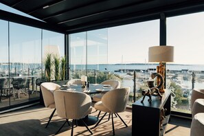A modern dining area with a panoramic view of a marina and cityscape. - Grand Hotel Åsgårdstrand - Unike Hoteller (Horten)