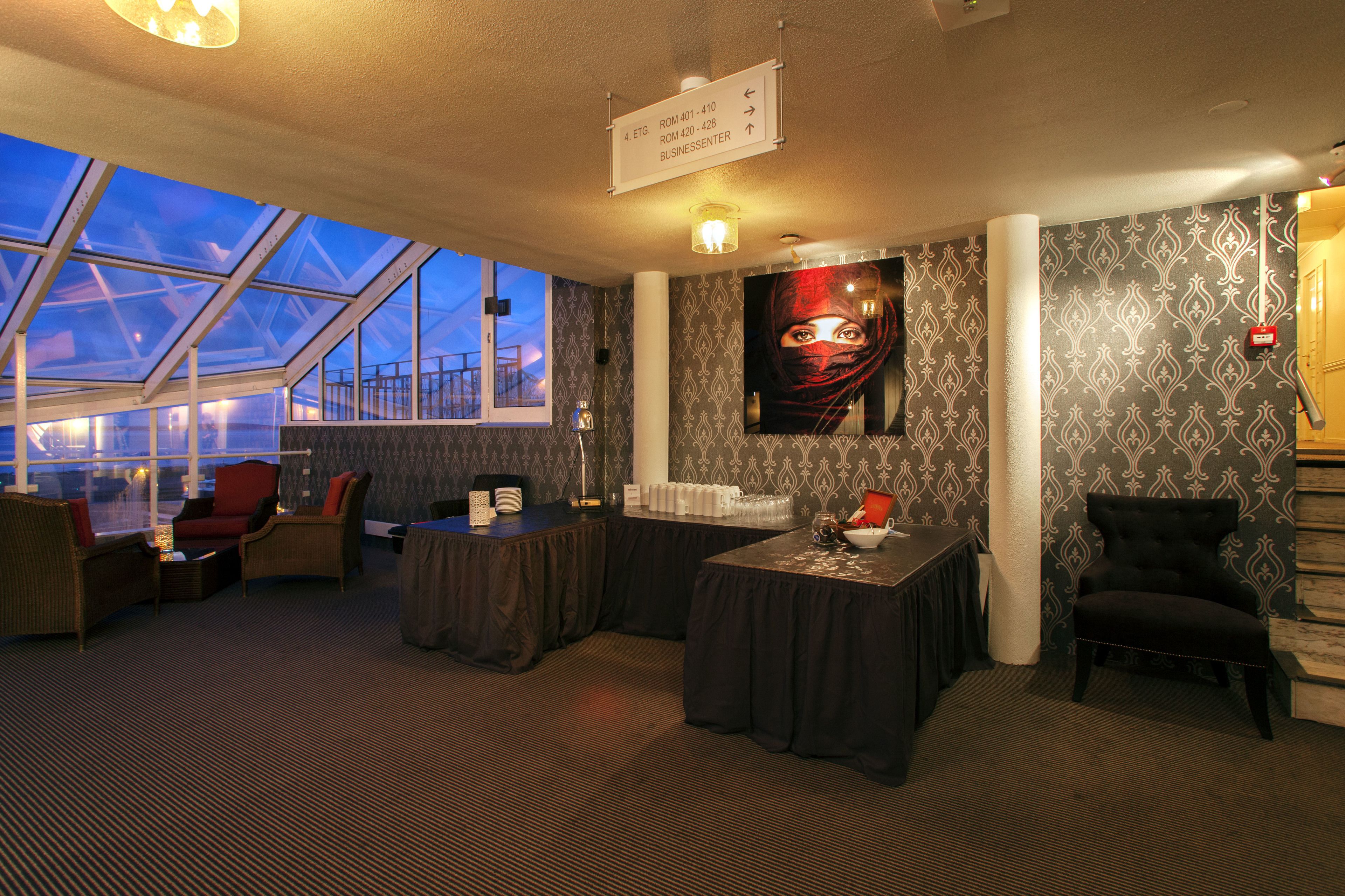 A modern hotel room with a large window, a comfortable seating area, a business center, and a staircase.