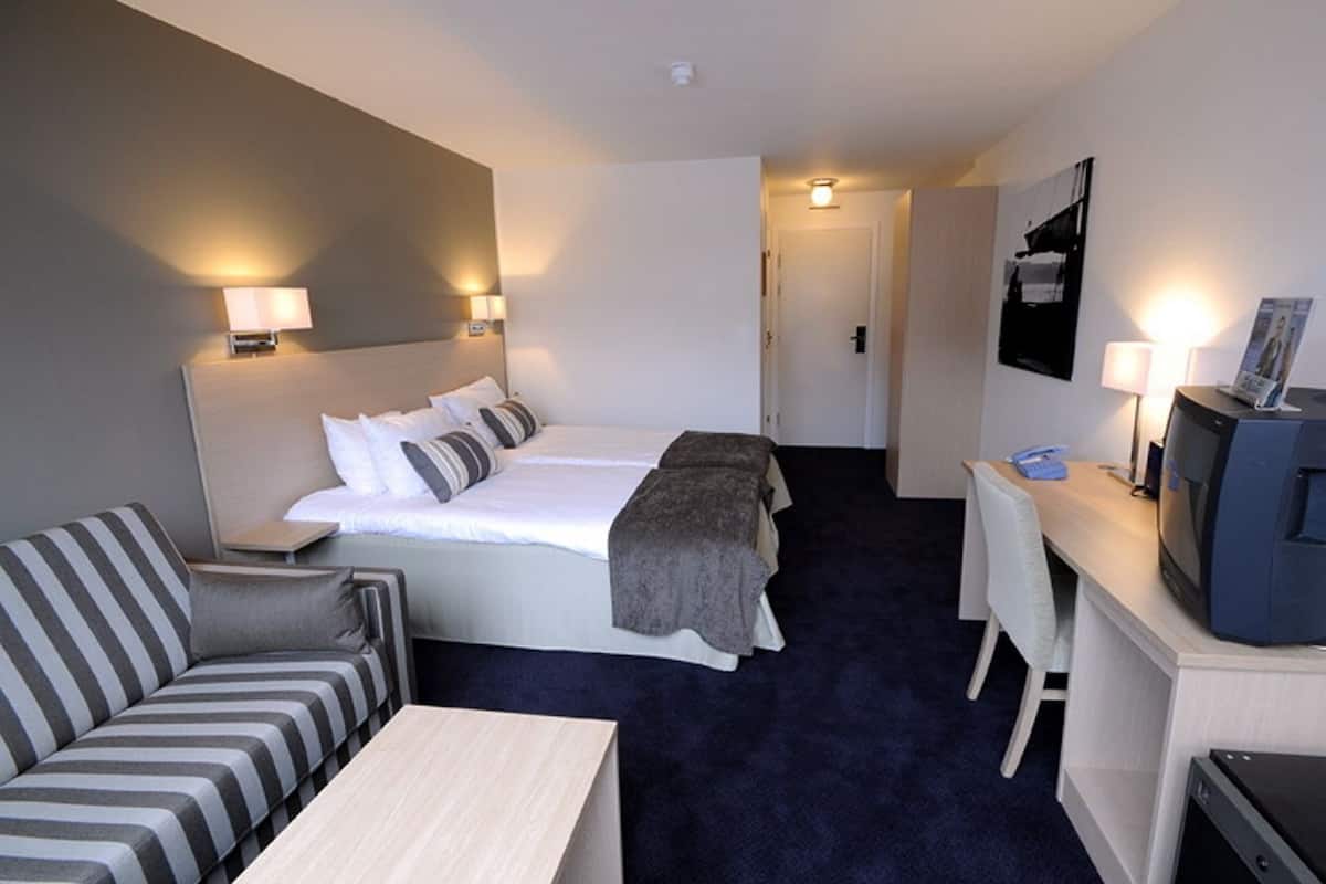 A hotel room with a bed, a sofa, a desk with a computer, and a TV.