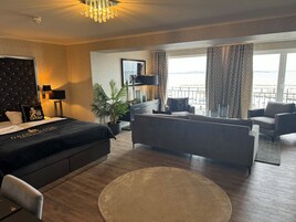 Una habitación de hotel moderna con una cama, dos sofás, una mesa de comedor y un ventanal con vistas.