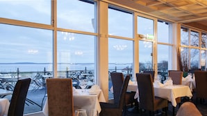 A restaurant with tables set for dining, large windows offering a view of the water and boats, and a ceiling with recessed lighting. - Grand Hotel Åsgårdstrand - Unike Hoteller (Horten)