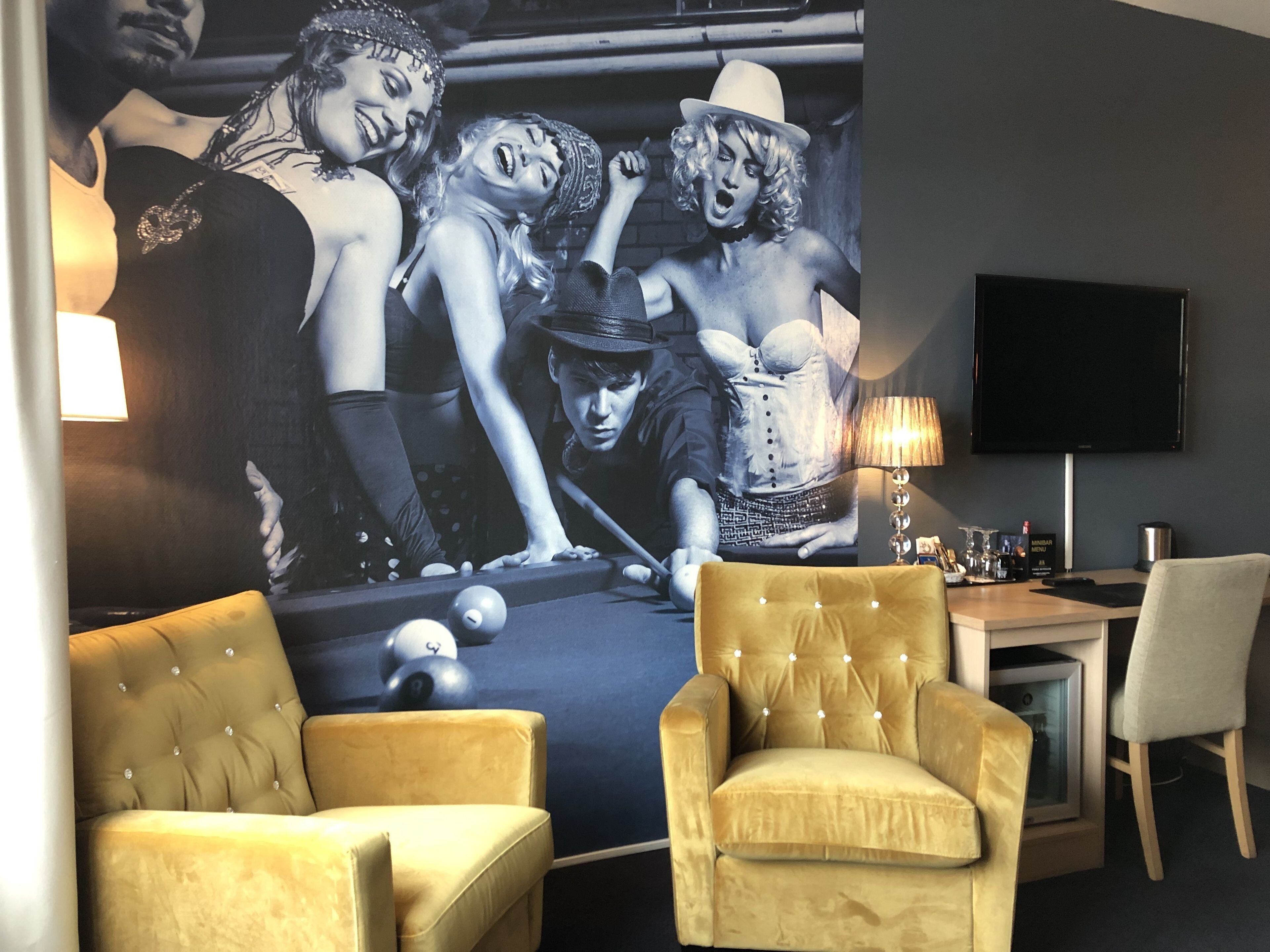 Una habitación con una mesa de billar, dos sillones amarillos, un televisor de pantalla plana y un mural en la pared.