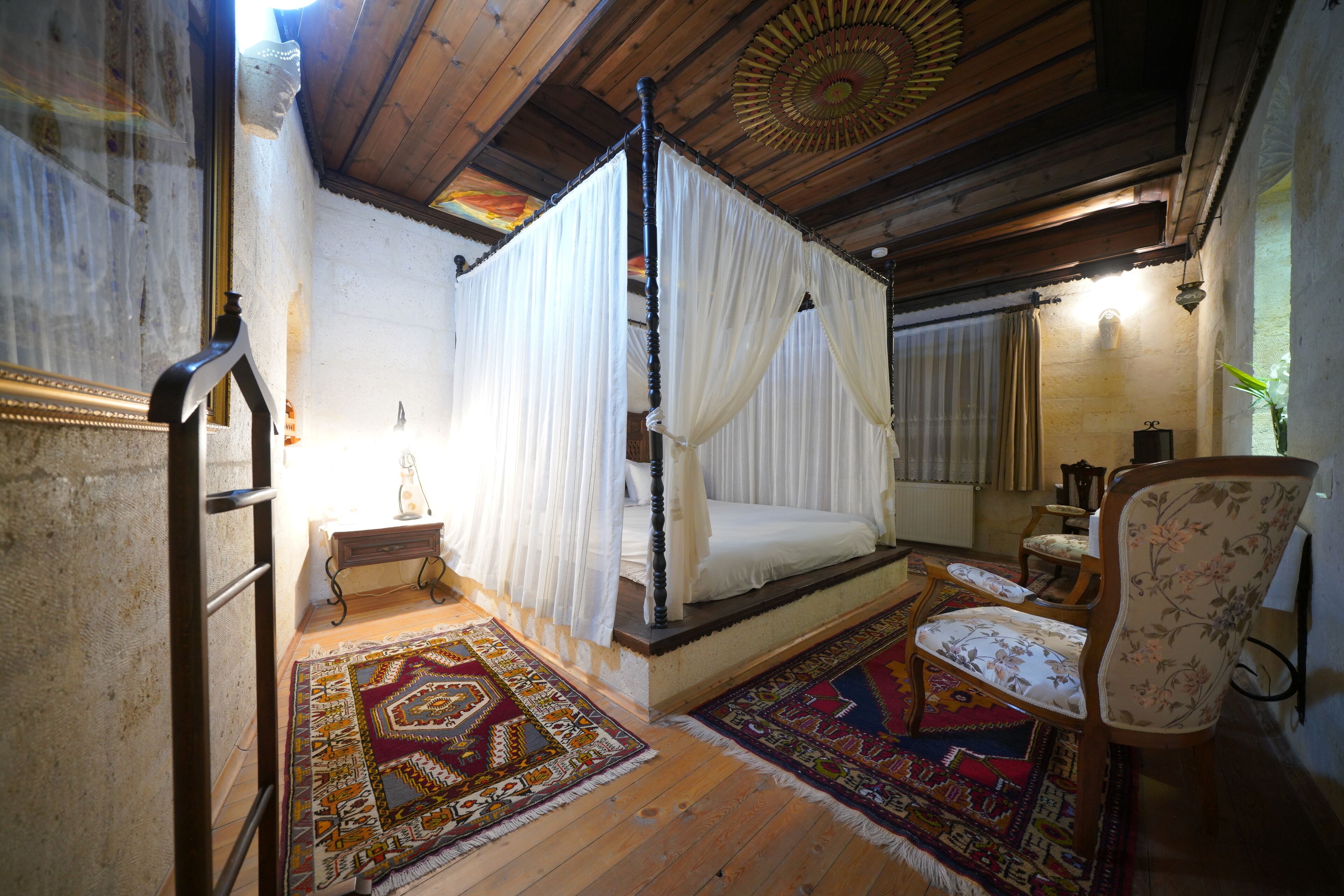 A traditional four-poster bed with white linens, a wooden floor, and a patterned rug.