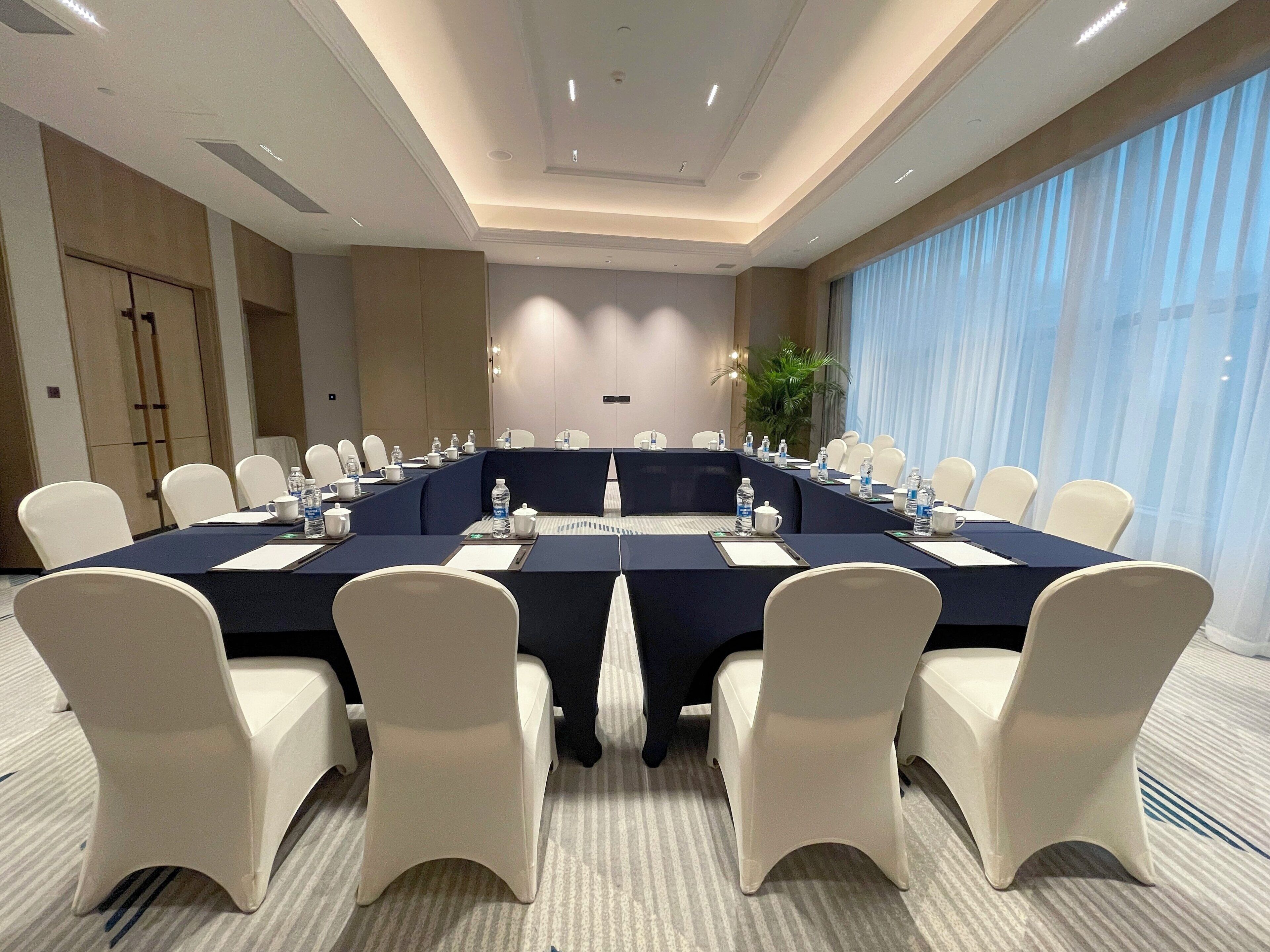 A conference room with a long table, white chairs, and a large window with curtains.