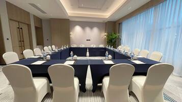 A conference room with a long table, white chairs, and a large window with curtains.