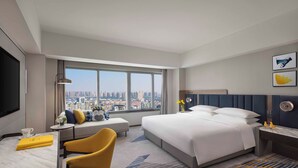 Una habitación de hotel moderna con una cama grande, un sofá, un escritorio y vistas a la ciudad.
