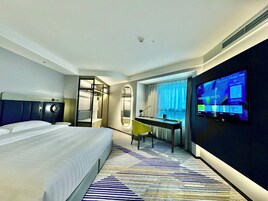A hotel room with a bed, desk, chair, TV, and a mirror.