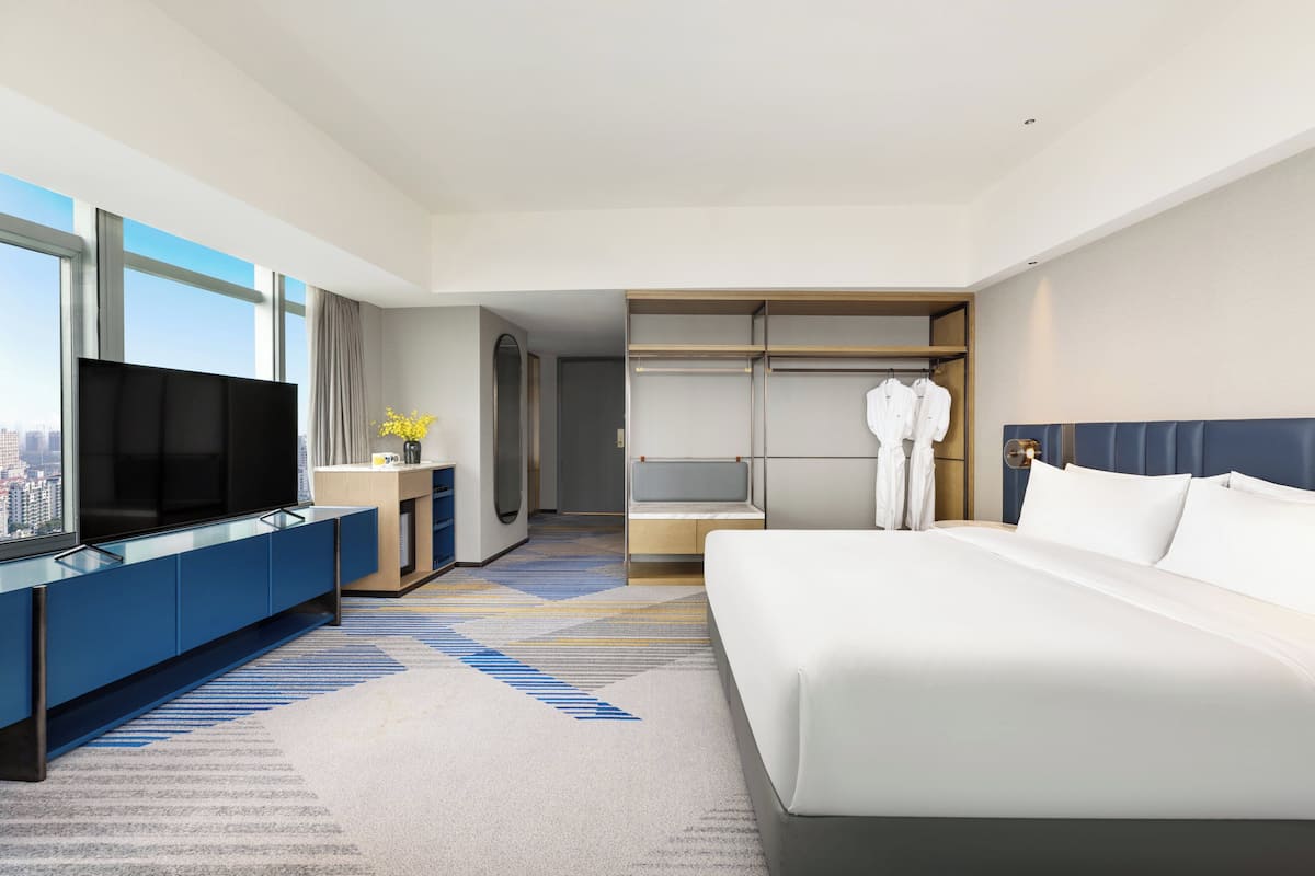 Habitación de hotel con cama, televisor, armario y vistas a la ciudad.