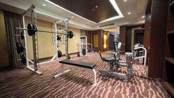 Un gimnasio de hotel con zona de pesas, una prensa de banca y un espejo instalado en la pared.