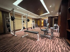Un gimnasio de hotel con zona de pesas, una prensa de banca y un espejo instalado en la pared.