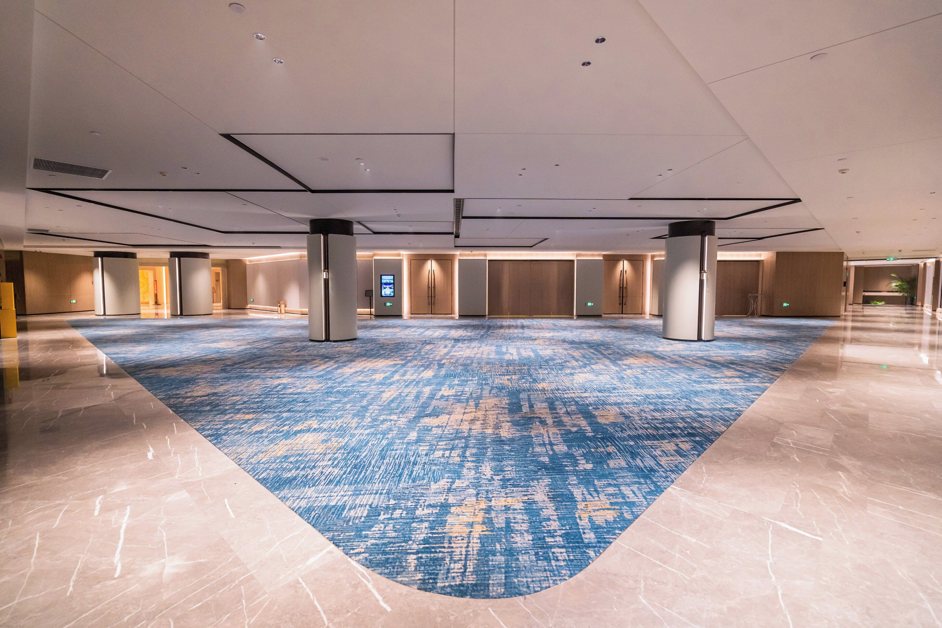 A spacious indoor area with a patterned carpet, large pillars, and a modern ceiling design.