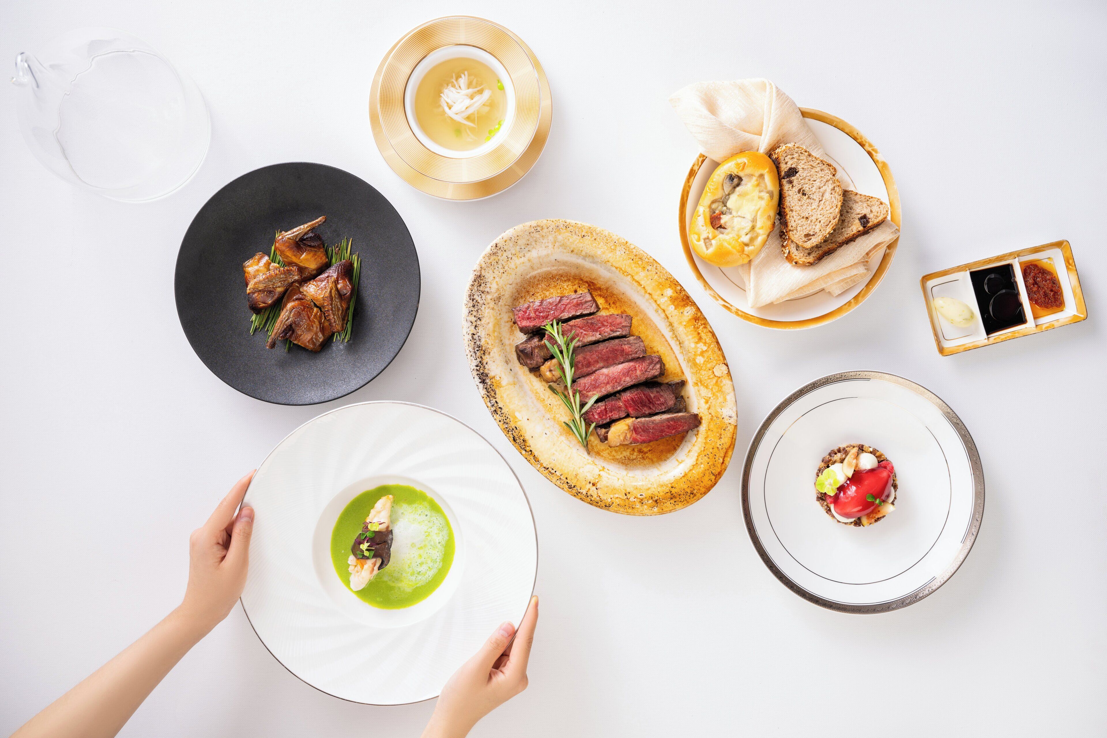 A dining table with various dishes, including a plate with meat, a bowl of soup, and a plate with bread.