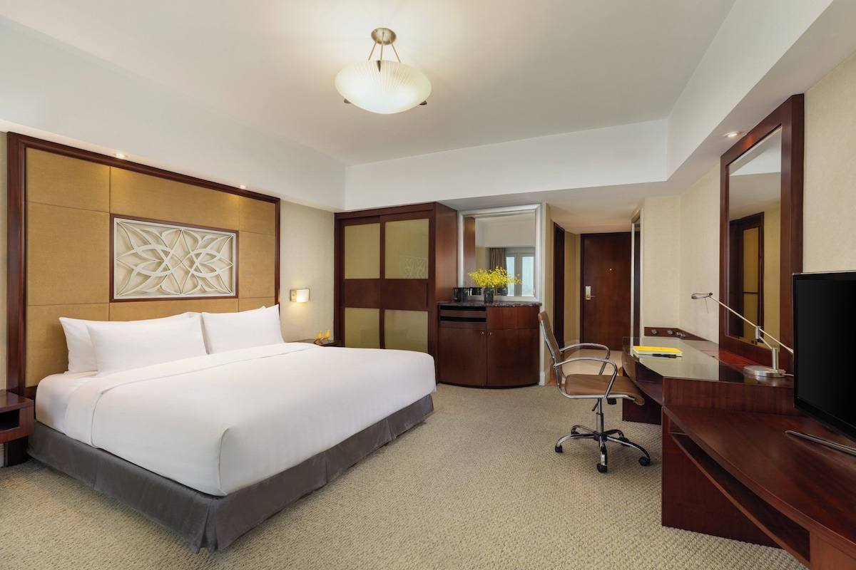 Quarto de hotel com uma cama grande, uma escrivaninha, uma cadeira, uma televisão e um espelho.