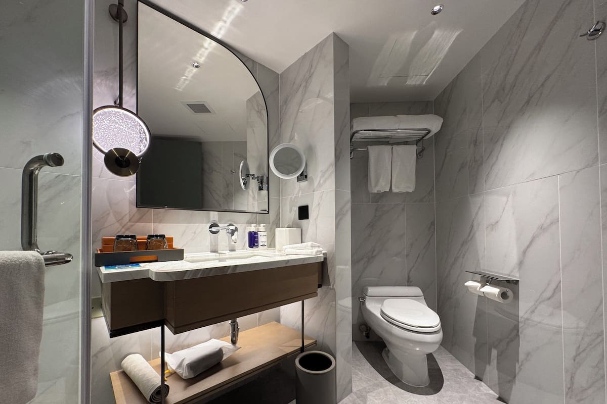 Un baño moderno con ducha acristalada, tocador con espejo, inodoro y un cubo de basura.