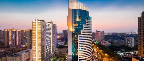 Un edificio alto con un diseño curvo único, rodeado de otros edificios altos en un entorno urbano.