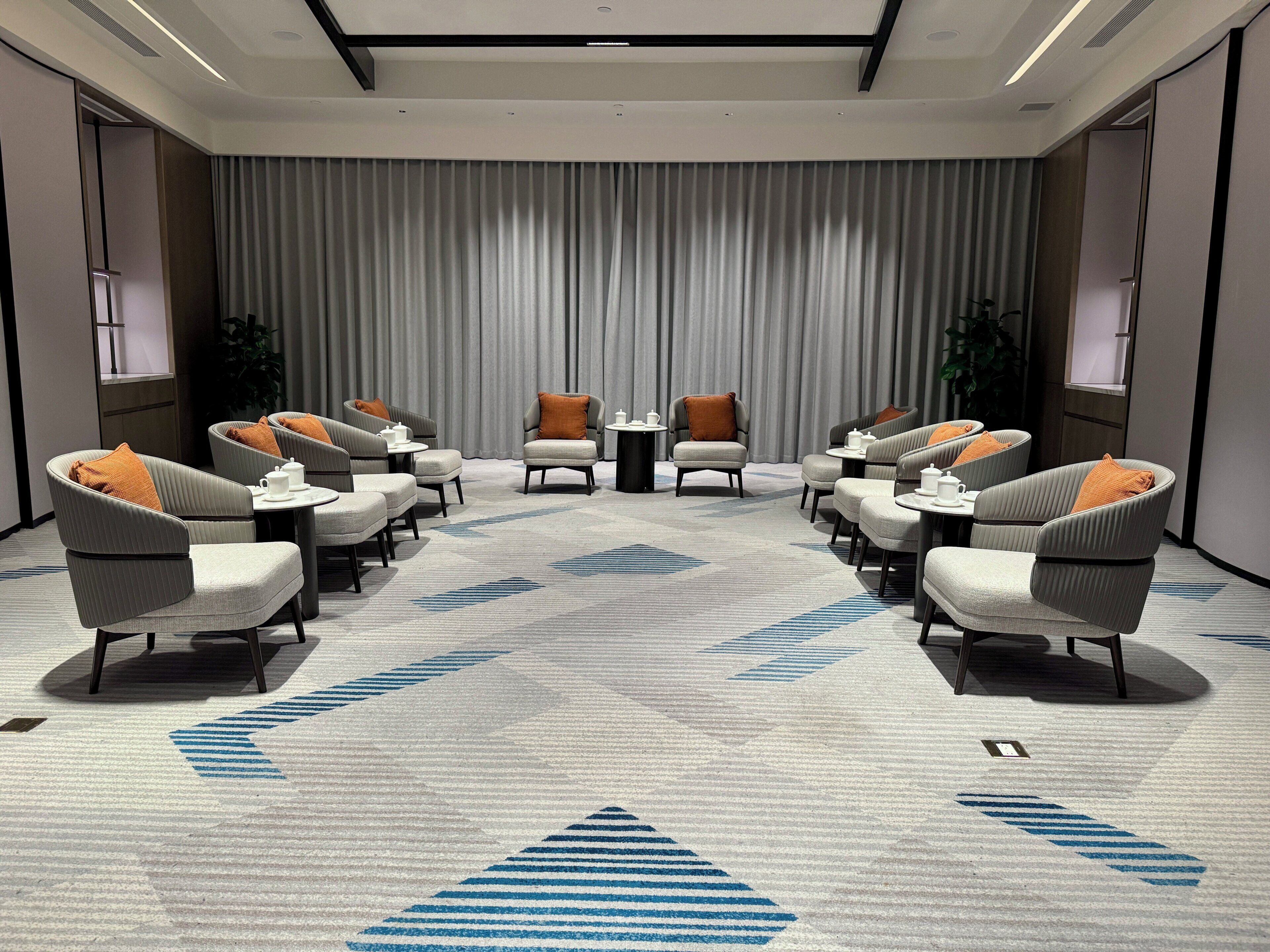A conference room with a long table and chairs, a patterned carpet, and a curtain backdrop.