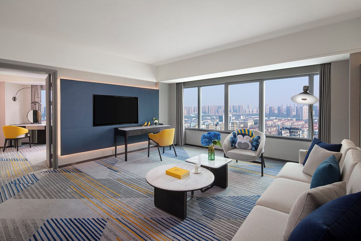 Una sala moderna con vista a la ciudad, un televisor de pantalla plana, un sofá, una mesa de centro y un comedor con sillas.
