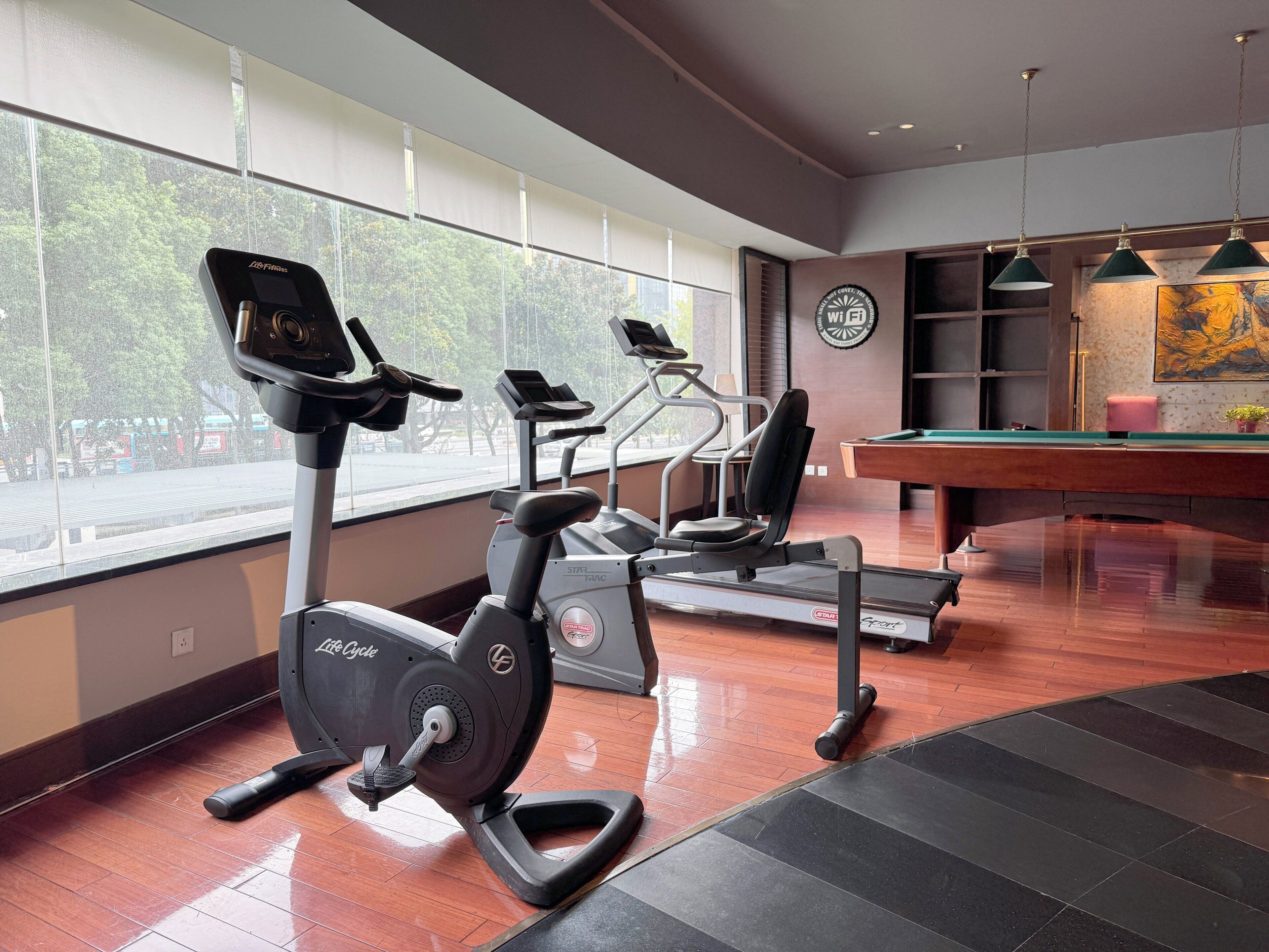 Un gimnasio con equipo de ejercicio, mesa de billar y ventanas amplias.