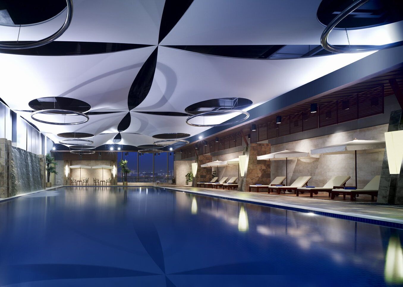 A modern indoor swimming pool with a clear view of the cityscape at night.