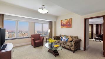 Habitación de hotel con un ventanal grande, un sofá, una mesa de centro de vidrio, un sillón rojo y una televisión.
