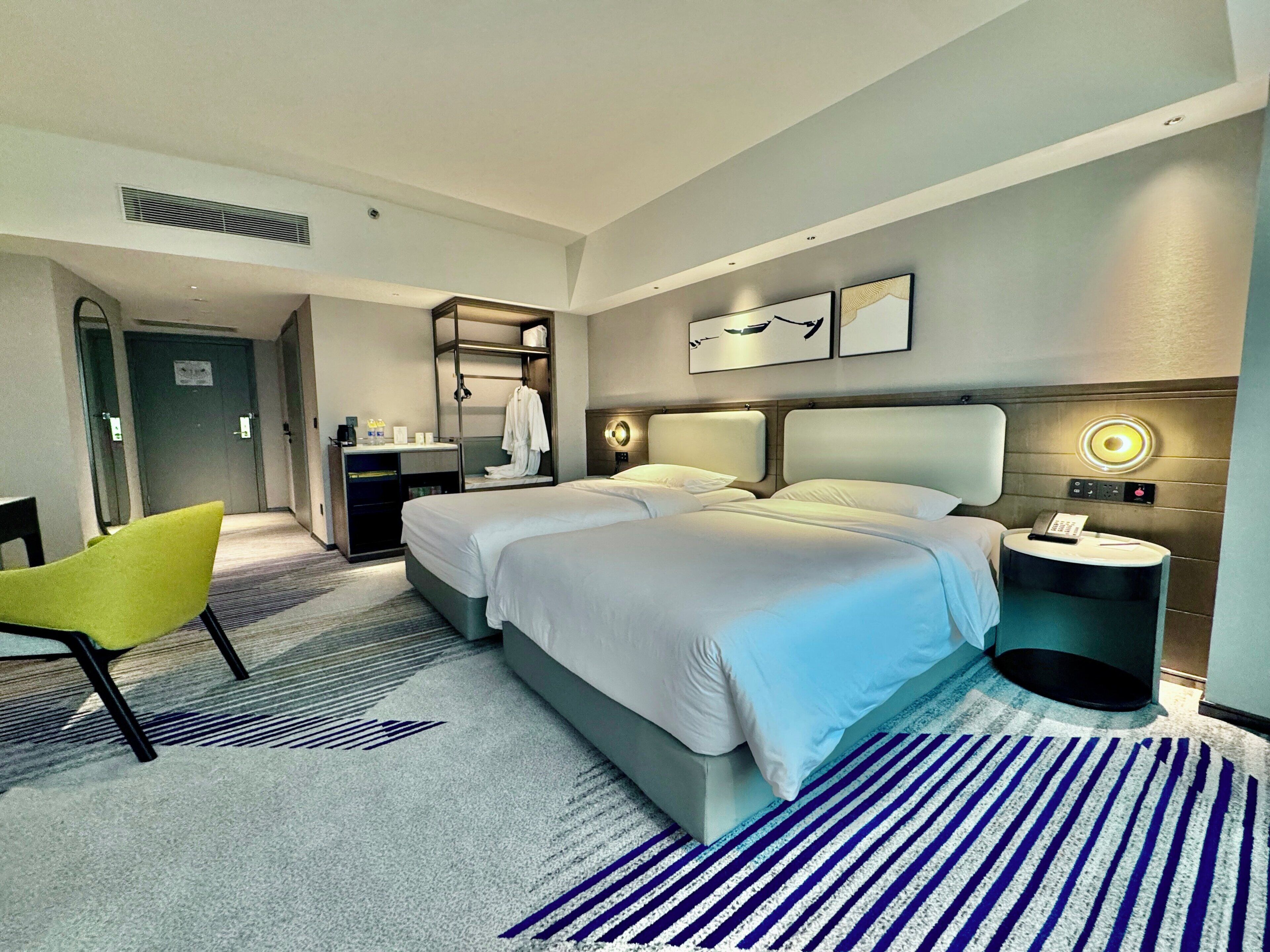 A hotel room with two beds, a desk, a chair, a bedside table, and a wall-mounted phone.