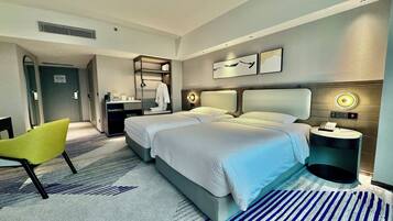A hotel room with two beds, a desk, a chair, a bedside table, and a wall-mounted phone.