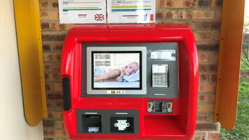 A red self-service kiosk with a screen displaying a message about a closed reception desk and instructions for guests.