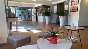 A modern hotel lobby with a seating area, a reception desk, and a large window. - Brit Hotel Essentiel Tours Sud – Chambray-lès-Tours  (Chambray-les-Tours)