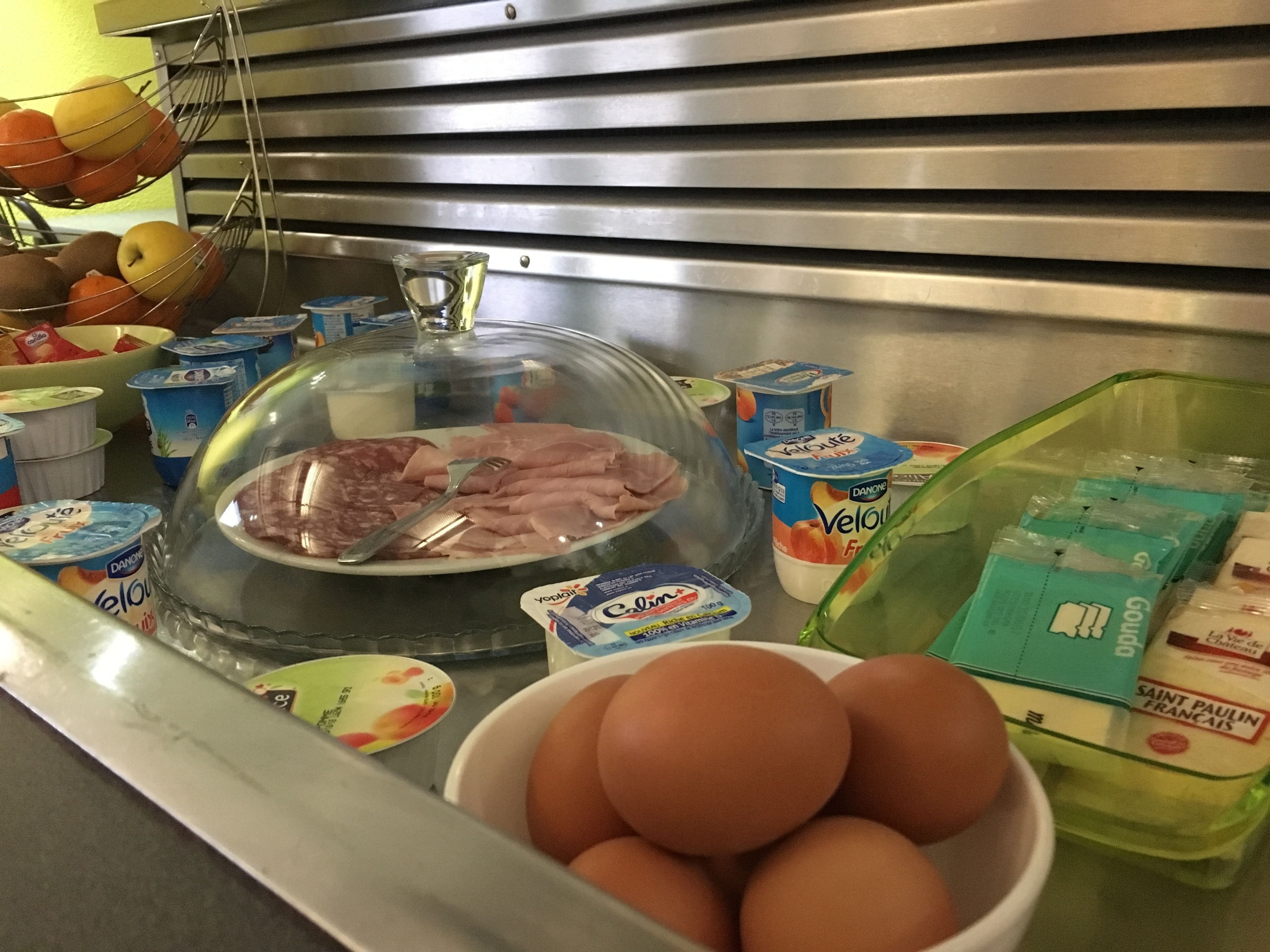 Un bancone della cucina con diversi alimenti, tra cui un piatto di carne a fette, una ciotola di uova e diversi vasetti di yogurt.